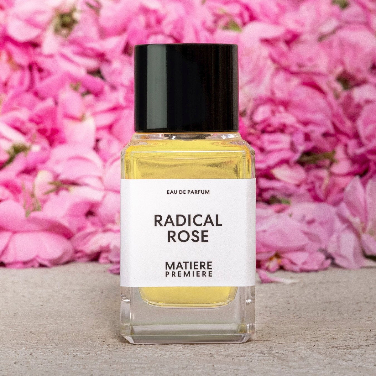 Perfume bottle labeled 'Radical Rose' by Matiere Premiere with pink flowers in the background