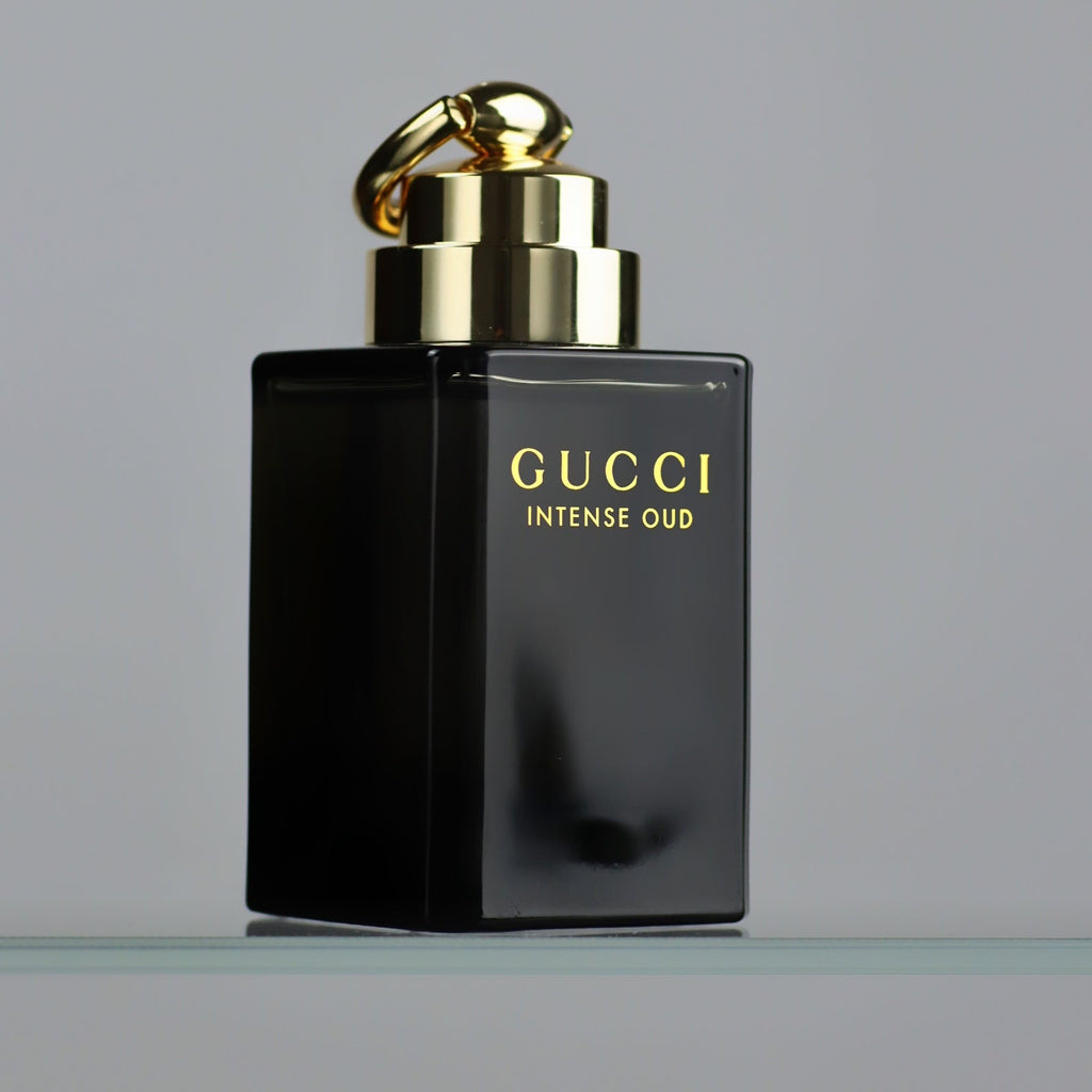 Black Gucci Intense Oud perfume bottle with gold cap on a gray background