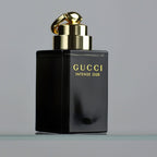 Black Gucci Intense Oud perfume bottle with gold cap on a gray background
