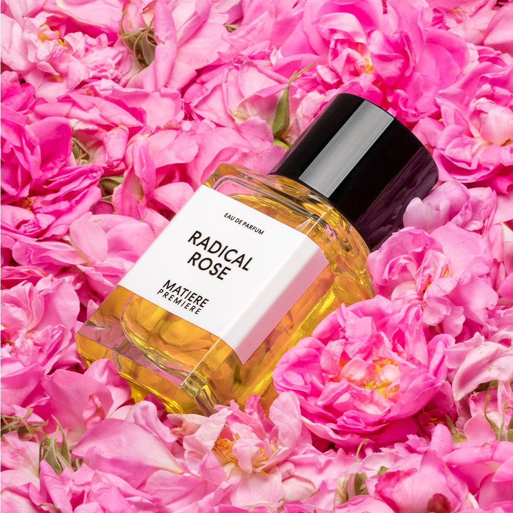 Perfume bottle labeled 'Radical Rose' by Matiere Premiere with pink flowers in the background