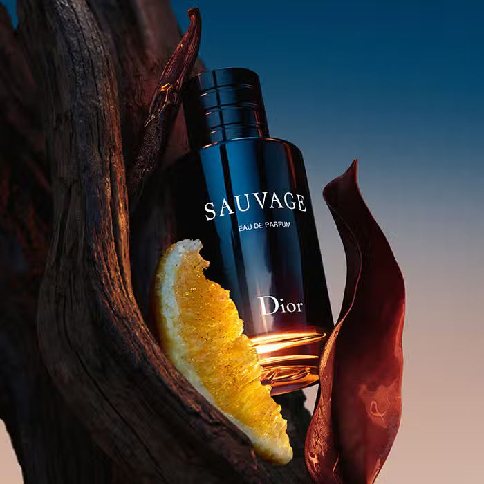 Dior Sauvage perfume bottle with orange slice and leaves on a gradient background